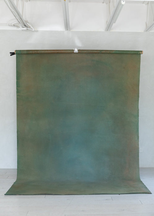 Emerald and teal hand painted Ultraviolet backdrop hangs on a c-stand in a natural light studio.