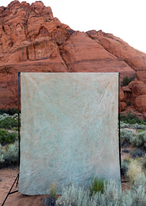 Image of gold, green, and beige huge muslin Ultraviolet backdrop hanging clipped to a traditional backdrop stand in Utah's Snow Canyon. Ultraviolet Backdrops are hand painted one of a kind and our Backdrops in a Bag fold or roll neatly into a bag for easy transportation and use for photographers, stylists, and other creative professionals and content creators.