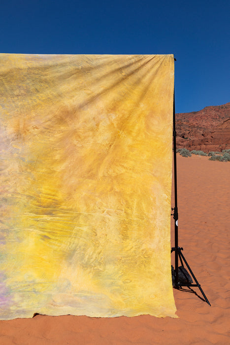 Yellow, marigold backdrop hand painted on lightweight muslin hangs on sand dunes in Utah. Backdrop in a Bag allows you to create a studio any where. 