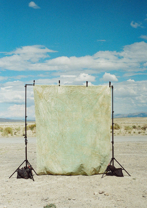 Image of gold, green, and beige huge muslin backdrop hanging clipped to a traditional backdrop stand in the west desert of Utah. Ultraviolet Backdrops are hand painted one of a kind and our Backdrops in a Bag fold or roll neatly into a bag for easy transportation and use for photographers, stylists, and other creative professionals and content creators. Image is shot on Lomography 800 film.