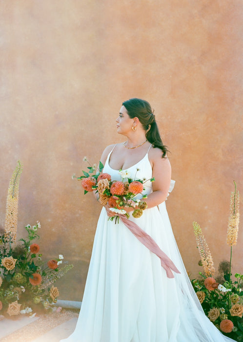 Bride stands against a yellow and pink backdrop with flowers