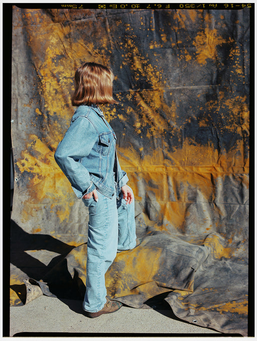Person wearing a denim outfit standing against a textured, multicolored backdrop