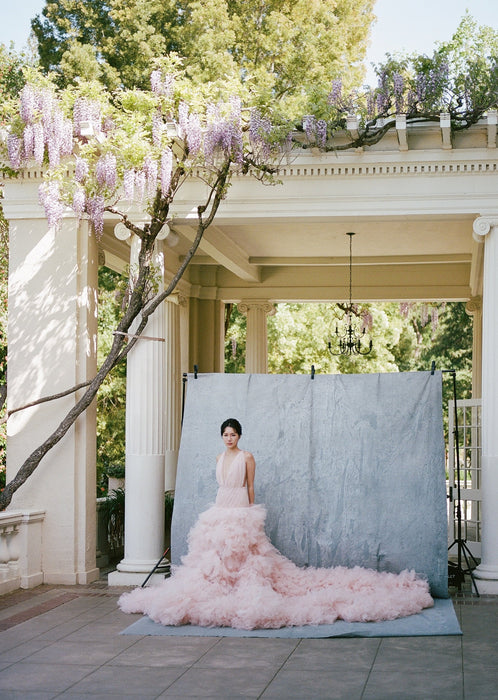 Image of bride wearing large light pink wedding gown shot by Simon Kim against Ultraviolet Backdrops big muslin Backdrop in a Bag called Neutral Giant. Backdrop is clipped using clamps to a sandbagged backdrop stand. Location is Montalvo Villa in Saratoga California. Backdrop in a Bag is a highly mobile on the go background for photographers who need backdrops that are easy to set up, travel-friendly and lightweight.  This image was shot on Kodak Portra 400 film. 