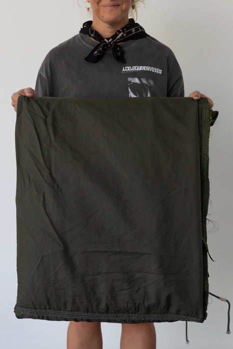Person holding a large green backdrop against a plain background in a photo studio. 